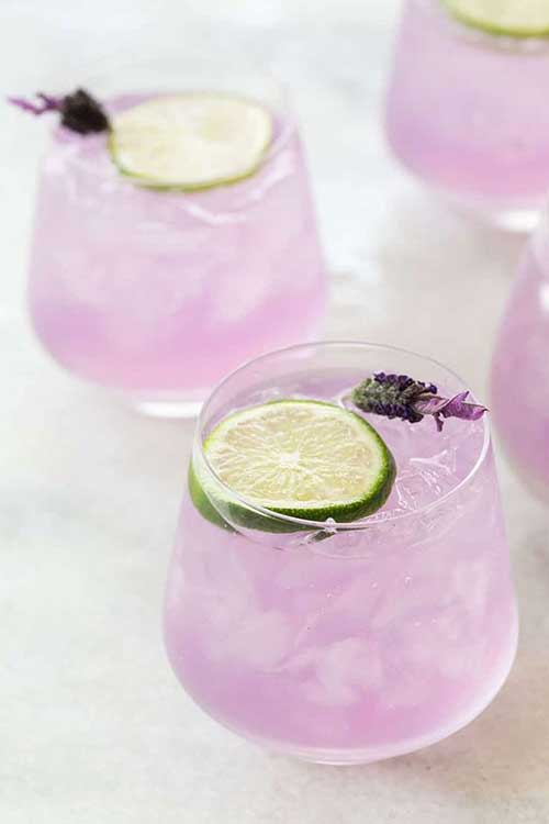 A Gin and Tonic infused with Lavendar in a glass served over ice and garnished with a lime wedge and dried lavendar