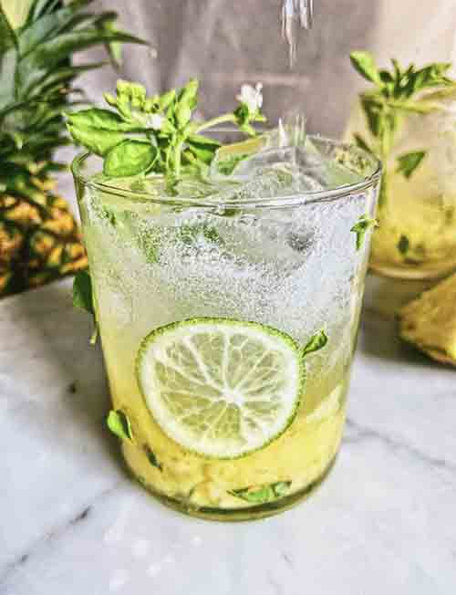 A Gin and Tonic infused with Pinaplle and Basil in a glass served over ice and garnished with mint and limes