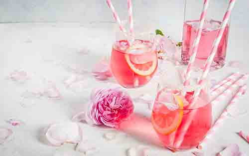 A Gin and Tonic infused with Rose petals in a glass served over ice and garnished with a lemon slices