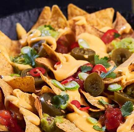 A close up of a plate of nachos with cheese on.